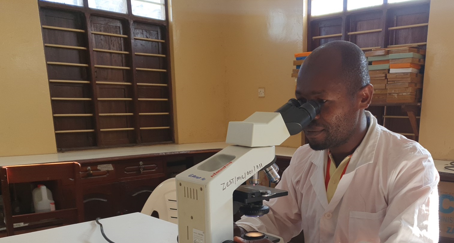 A lab technician in Zanzibar examines snails under a microscope.
